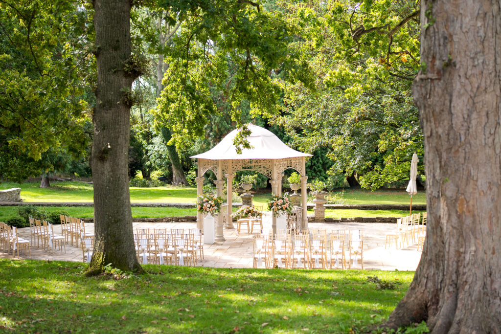 Outdoor ceremony at Eastington Park decorated with 2 large urns of flowers in Toffee tones for an autumn wedding