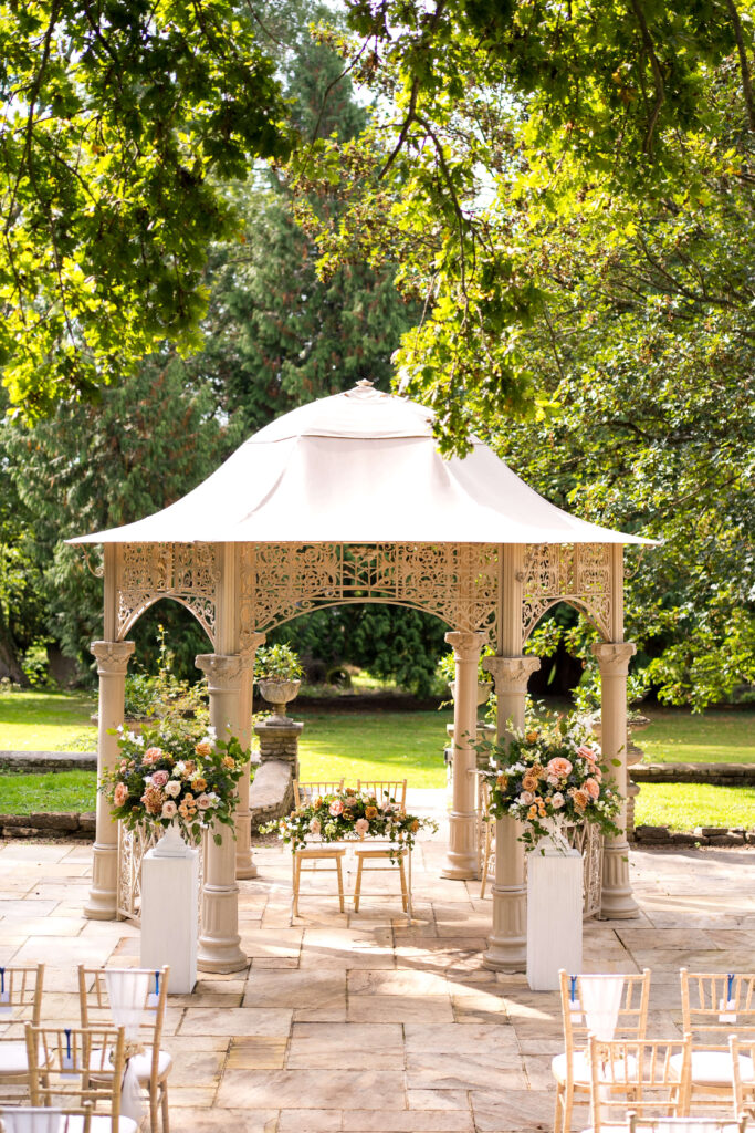 Outdoor ceremony at Eastington Park decorated with 2 large urns of flowers in Toffee tones for an autumn wedding