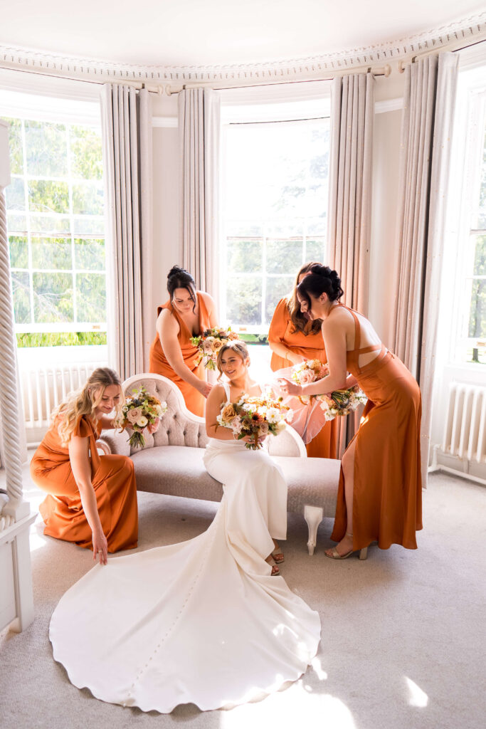 Bridesmaid in satin rust coloured dresses holding bouquets of flowers in autumn shades