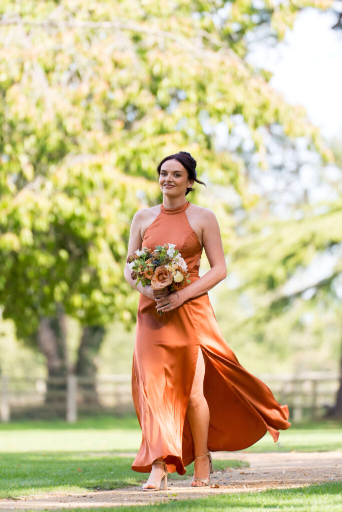 Bridesmaid in satin rust coloured dresses holding bouquets of flowers in autumn shades